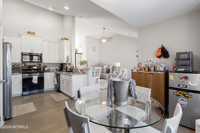 dining space with sink, high vaulted ceiling, light wood-type flooring, and ceiling fan