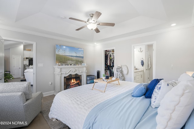 bedroom with ornamental molding, ensuite bathroom, a tray ceiling, and ceiling fan