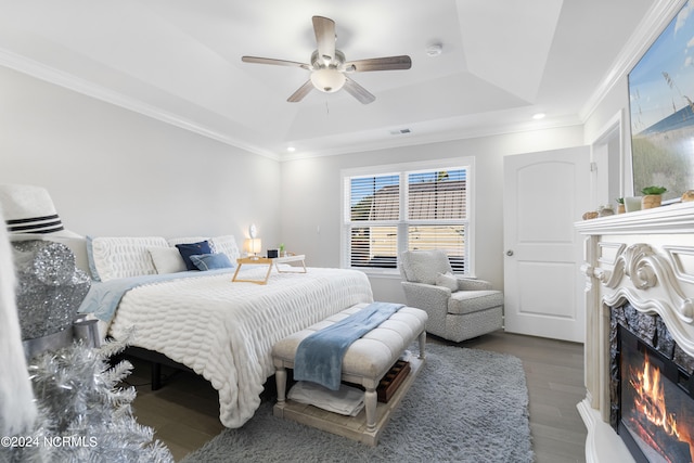 bedroom with a tray ceiling, a high end fireplace, hardwood / wood-style floors, ornamental molding, and ceiling fan