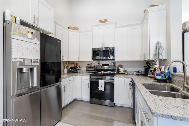 kitchen with light stone countertops, sink, stainless steel appliances, white cabinets, and light hardwood / wood-style flooring