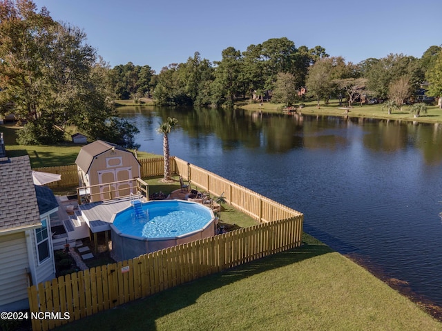 view of swimming pool with a shed, a yard, and a water view