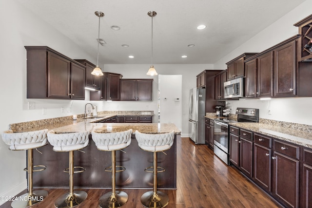 kitchen featuring sink, a kitchen bar, stainless steel appliances, decorative light fixtures, and dark wood-type flooring