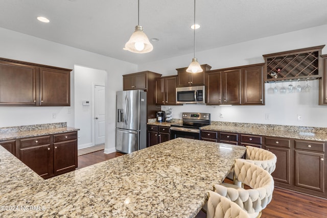 kitchen featuring hanging light fixtures, a breakfast bar area, appliances with stainless steel finishes, dark hardwood / wood-style flooring, and dark brown cabinetry