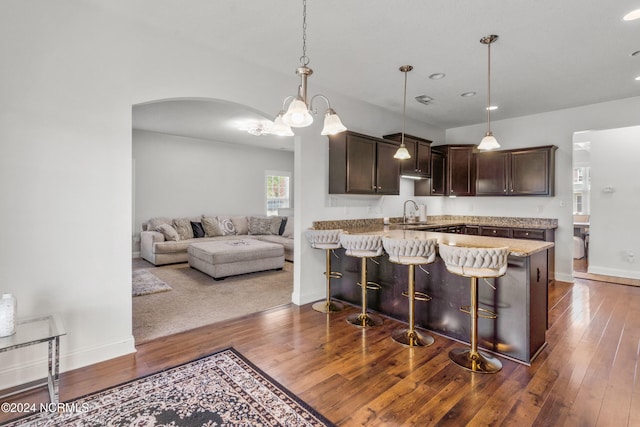 kitchen with dark brown cabinets, a kitchen breakfast bar, dark wood-type flooring, sink, and decorative light fixtures