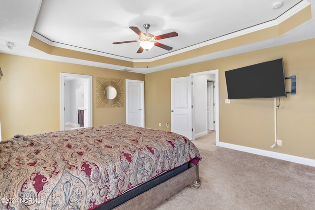 bedroom with a raised ceiling, ceiling fan, crown molding, ensuite bath, and light colored carpet