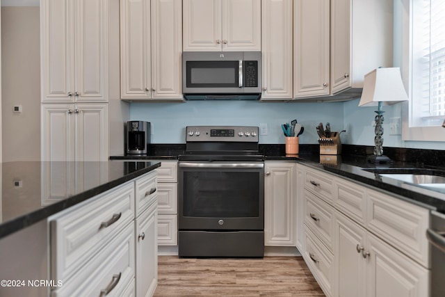 kitchen with stainless steel appliances, white cabinetry, dark stone counters, and light hardwood / wood-style flooring