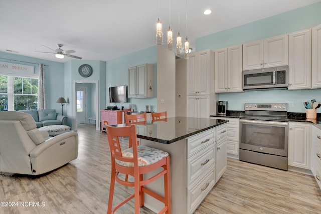 kitchen with appliances with stainless steel finishes, a kitchen breakfast bar, ceiling fan with notable chandelier, light hardwood / wood-style floors, and a kitchen island