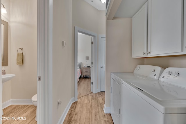 laundry area featuring washer and dryer, light wood-type flooring, and cabinets