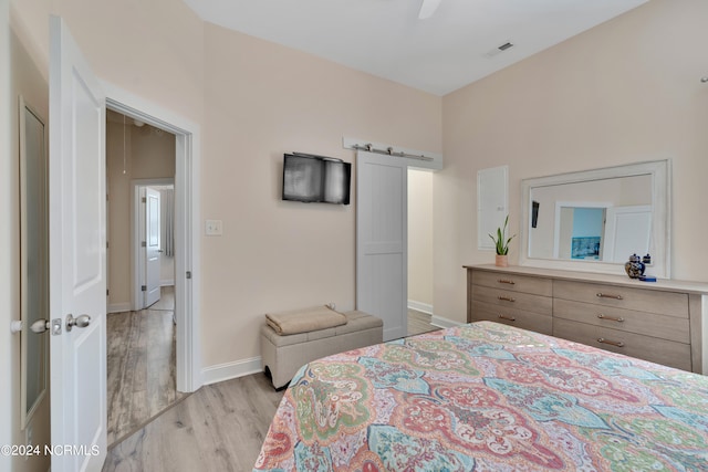 bedroom featuring a barn door, ceiling fan, and light hardwood / wood-style floors