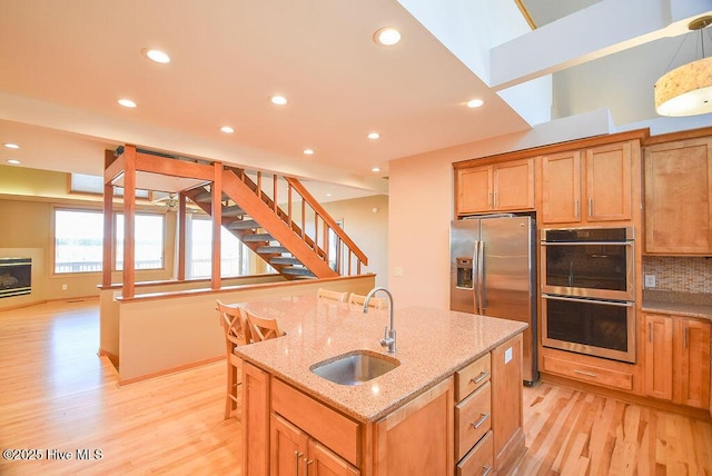 kitchen with sink, decorative light fixtures, light stone counters, a kitchen island with sink, and appliances with stainless steel finishes