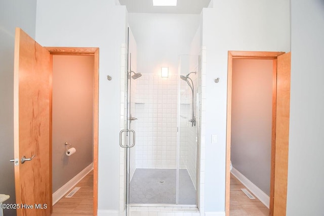 bathroom with hardwood / wood-style floors, a shower with shower door, and toilet