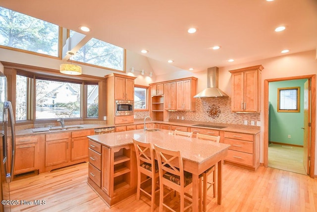 kitchen with appliances with stainless steel finishes, an island with sink, light stone counters, decorative backsplash, and wall chimney range hood