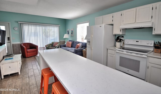 kitchen featuring a kitchen breakfast bar, white cabinetry, dark hardwood / wood-style floors, range hood, and white appliances