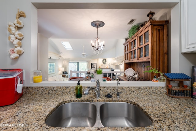 kitchen with pendant lighting, visible vents, a sink, light stone countertops, and vaulted ceiling with skylight