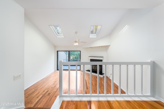 spare room with a fireplace with flush hearth, lofted ceiling with skylight, wood finished floors, and a ceiling fan