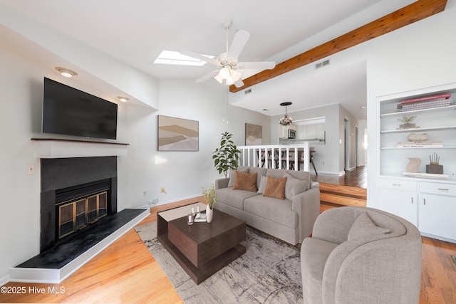 living area featuring a glass covered fireplace, baseboards, visible vents, ceiling fan, and wood finished floors