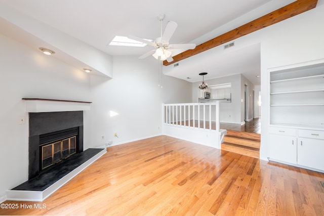 unfurnished living room with visible vents, baseboards, a glass covered fireplace, ceiling fan, and light wood-type flooring