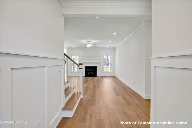 unfurnished living room with ornamental molding, a large fireplace, light wood-type flooring, and ceiling fan