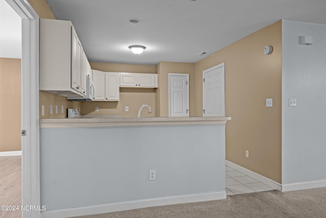 kitchen featuring light carpet, sink, kitchen peninsula, and white cabinets