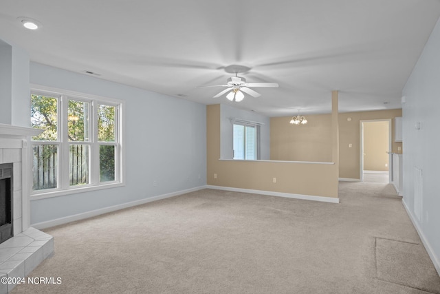 unfurnished living room with light carpet, a fireplace, and ceiling fan with notable chandelier