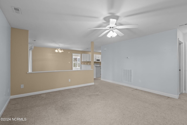 spare room featuring ceiling fan with notable chandelier and light colored carpet