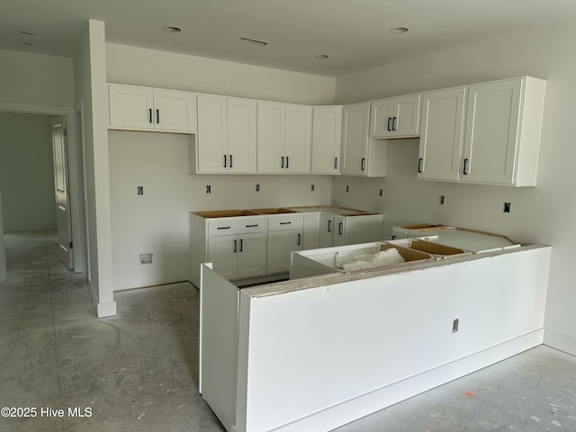 kitchen with baseboards, concrete floors, white cabinetry, and visible vents