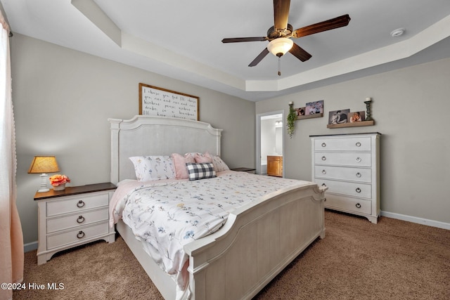 carpeted bedroom with ceiling fan, ensuite bathroom, and a tray ceiling