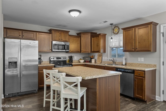 kitchen featuring stainless steel appliances, sink, dark hardwood / wood-style floors, a kitchen island, and hanging light fixtures