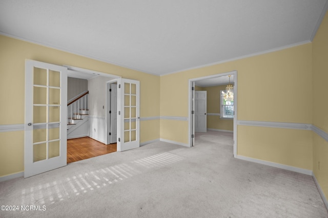 spare room featuring french doors, crown molding, carpet floors, and an inviting chandelier