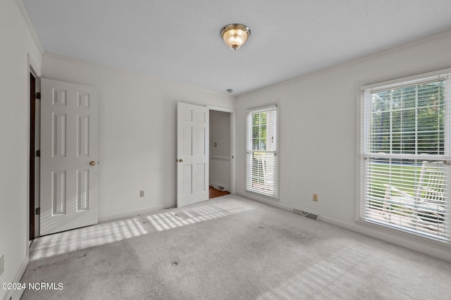 empty room featuring crown molding, plenty of natural light, and light colored carpet