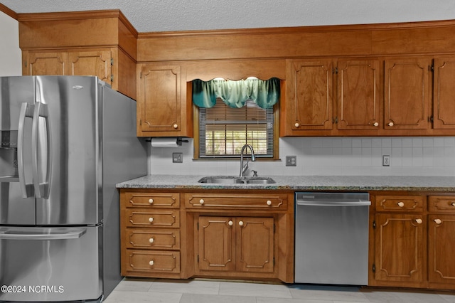 kitchen featuring tasteful backsplash, a textured ceiling, light stone countertops, sink, and stainless steel appliances