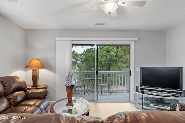 living room with a textured ceiling, light wood-type flooring, and ceiling fan