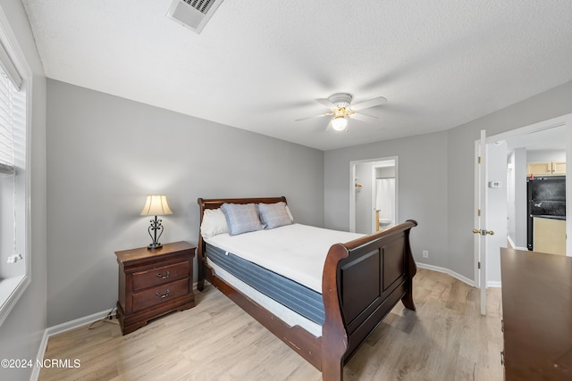 bedroom featuring ensuite bathroom, light wood-type flooring, a textured ceiling, black fridge, and ceiling fan