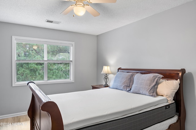 bedroom with a textured ceiling, light wood-type flooring, and ceiling fan