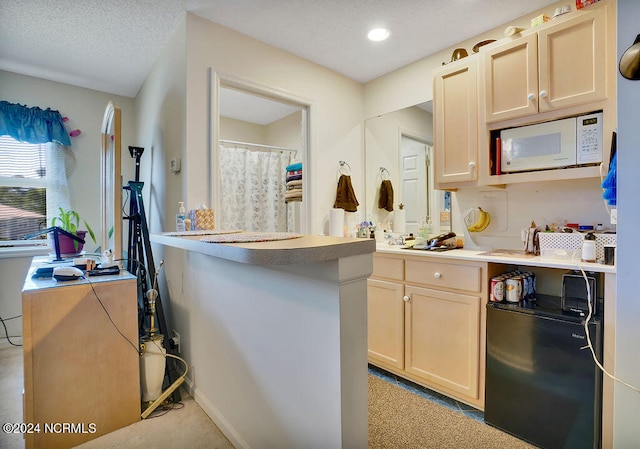 kitchen featuring black refrigerator, kitchen peninsula, light colored carpet, light brown cabinetry, and a textured ceiling