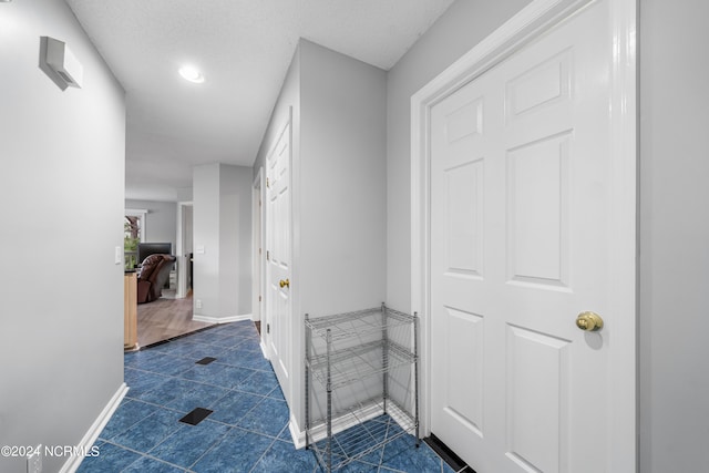 hall with a textured ceiling and dark tile patterned flooring