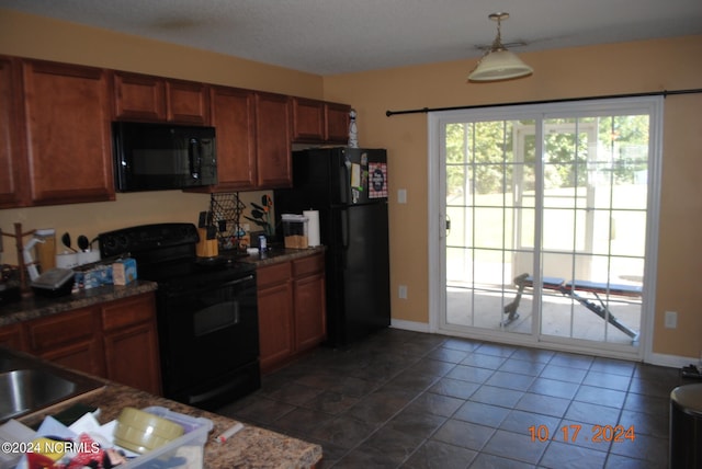 kitchen with dark stone countertops, black appliances, dark tile patterned floors, and hanging light fixtures