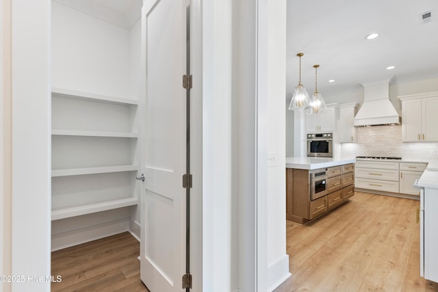 5312 Hanahan Dr, Wilmington, NC 28403 - kitchen featuring custom range hood, oven, light countertops, light wood-style flooring, and decorative backsplash