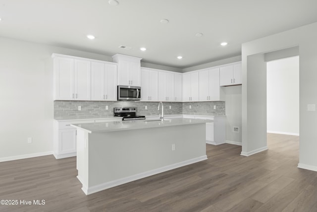 kitchen with white cabinetry, dark wood-type flooring, backsplash, a kitchen island with sink, and appliances with stainless steel finishes