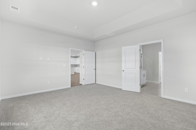 unfurnished bedroom featuring ensuite bathroom, a raised ceiling, and light colored carpet