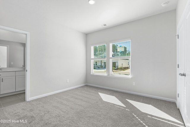 unfurnished bedroom featuring ensuite bathroom and light carpet