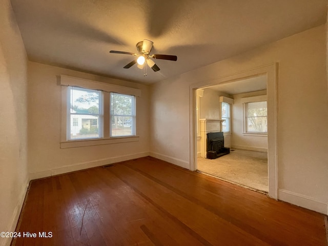 unfurnished living room featuring a wood stove, ceiling fan, plenty of natural light, and hardwood / wood-style flooring