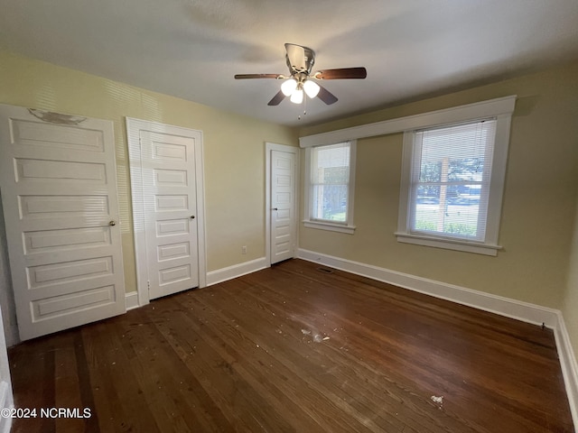 unfurnished bedroom featuring ceiling fan, dark hardwood / wood-style flooring, and multiple closets