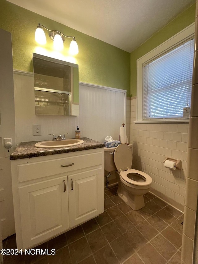 bathroom featuring walk in shower, tile patterned floors, toilet, vanity, and tile walls