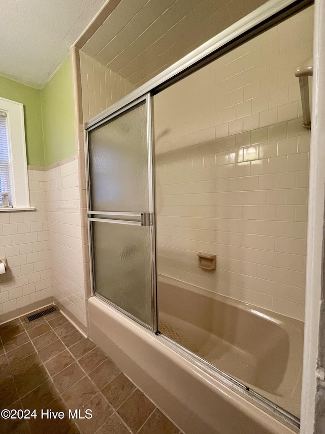 bathroom with tile patterned flooring, bath / shower combo with glass door, and tile walls