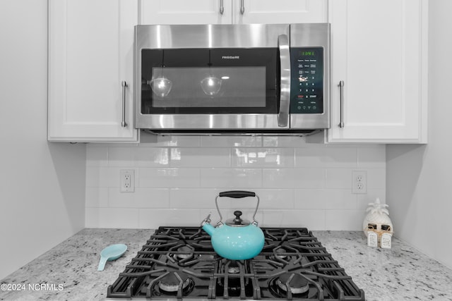 room details featuring white cabinetry, backsplash, and light stone countertops