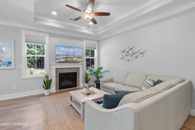 living room with a tiled fireplace, hardwood / wood-style floors, crown molding, a raised ceiling, and ceiling fan