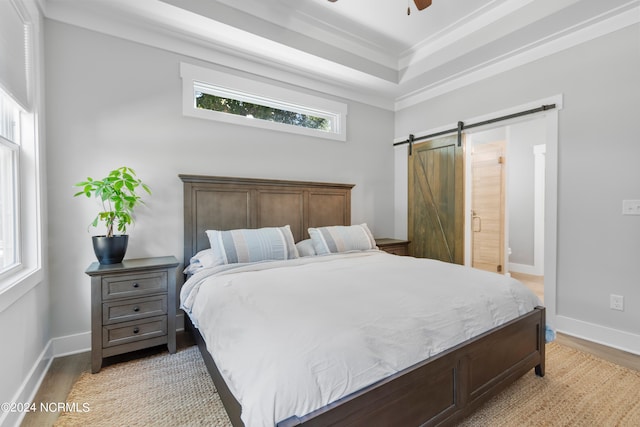 bedroom with ornamental molding, a barn door, light hardwood / wood-style flooring, and ceiling fan