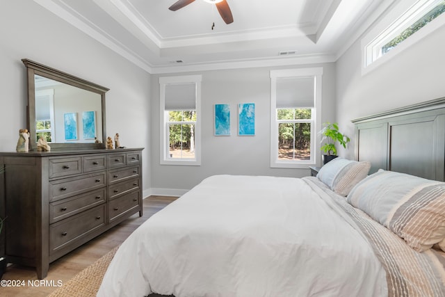 bedroom featuring ceiling fan, crown molding, a tray ceiling, and light wood-type flooring