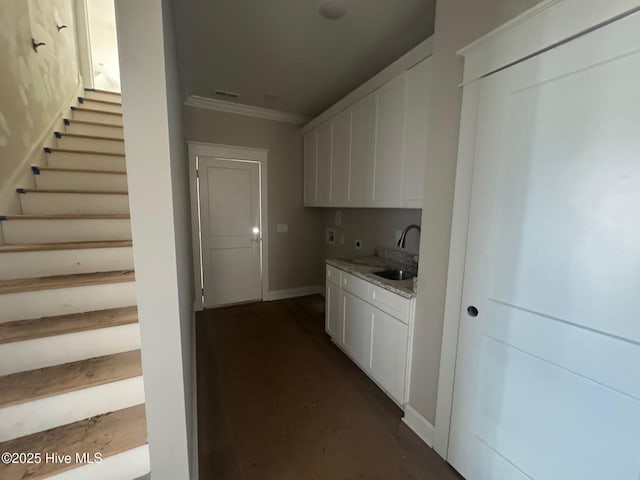 kitchen with crown molding, visible vents, white cabinets, a sink, and baseboards